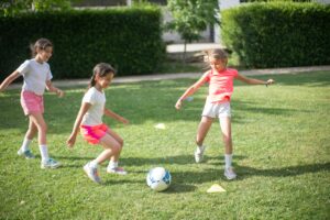 Three young girls having fun playing soccer outdoors on a sunny day.